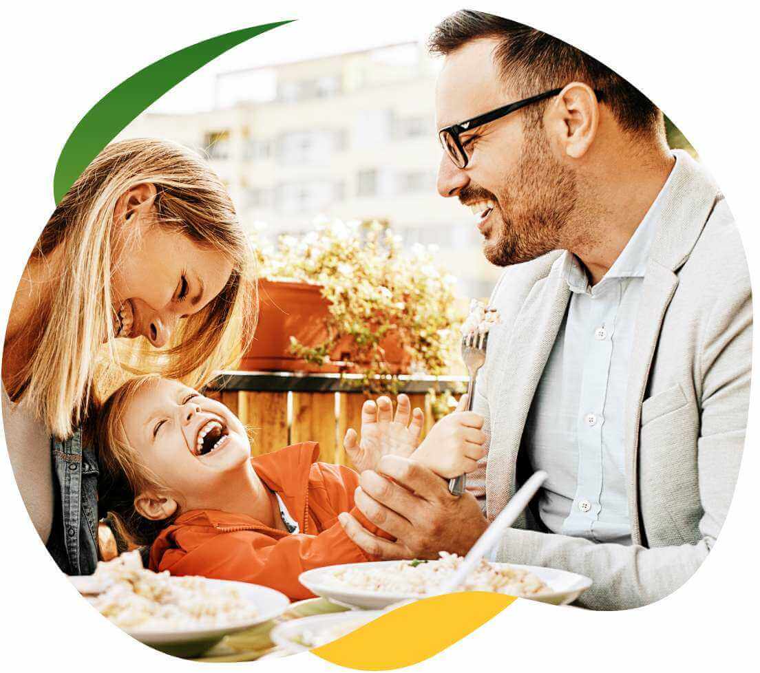 Młodzi rodzice jedzą posiłek przy stole, między nimi siedzi dziecko, śmieją się i dobrze razem bawią, ponieważ nie mają problemu ze wzdęciami dzięki Espumisan