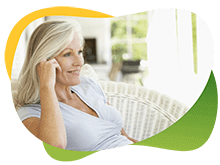 Zrelaksowana kobieta w średnim wieku siedzi na fotelu w schludnym salonie i rozmawia przez telefon, pomimo menopauzy, nie ma problemów ze wzdęciami dzięki Espumisan