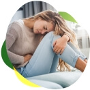 Młoda kobieta siedzi na łóżku, trzyma się za brzuch, cierpi z powodu wzdęć i gazów podczas miesiączki