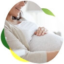 Siedząca kobieta w ciąży, trzyma dłonie na swoim brzuchu, uśmiecha się, ponieważ nie odczuwa wzdęć.
